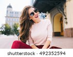 Cool girl with long hairstyle and vinous lips having fun in the city. She wears sunglasses and smiling to camera with snow-white smile.
