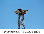 Four large public civil defence warning air sirens mounted on top of tall rusted metal structure on clear blue sky background