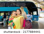 Small photo of Brazilian mother and daughter at the bus station with a big suitcase and ordinary colorful dress
