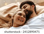 Small photo of In a scene of love and joy, a young couple lies together on a bed, laughing heartily. Their shared emotions and fun are palpable in this cozy, intimate moment, symbolizing deep affection
