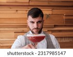 Small photo of Young bartender with a serious countenance with a cocktail in his hands. Concept: lifestyle, drinks, nightlife