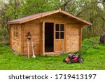 Garden shed with hoe, string trimmer,  rake and grass-cutter. Gardening tools shed. Garden house on lawn in garden. Wooden tool-shed. Hovel made of timber in domestic environment. 