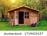 Small photo of Hovel after work in evening, golden hour. Garden shed (front view) with hoe, string trimmer, rake and grass-cutter. Gardening tools shed. Garden house on lawn in the sunset. Wooden tool-shed.