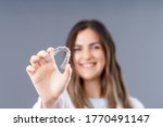Small photo of Beautiful smiling Turkish woman is holding an invisalign bracer in a grey background studio with copy space