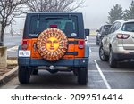 Small photo of 12-6-2018 Tulsa USA - Back of orange jeep stopped in traffic on grey winter day with bright sunshine wheel cover and Okie and OSU and CoExist stickers on back