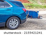 Small photo of Blue hatchback car parked on gravel with hitch cargo carrier holding tied down rubber storage box on back - Closeup and cropped