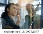 Small photo of Succeeding is top priority. Shot of a group of colleagues brainstorming together on a glass wall in an office.