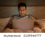 Hes a night owl. A young man working on his laptop in bed.