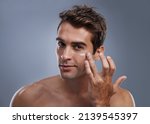 Small photo of Even men like to be soft..... Studio shot of a handsome young man applying cream to his face.
