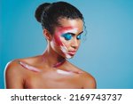 Small photo of Face paint bring forth her true nature. Studio shot of a beautiful young woman covered in face paint posing against a blue background.