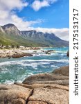 Small photo of Landscape view of ocean beach, sea, clouds, blue sky with copy space on Camps Bay, Cape Town, South Africa. Tidal waves washing on shoreline rocks or boulders. Background of Twelve Apostles mountains