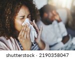 Ill or sick woman with allergy, sinus infection sneezing in tissue or blowing nose during flu season at home. Sick girl caught a bad cold showing symptoms of covid, or suffering from a virus disease