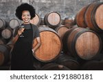 Portrait of a young woman winemaker standing with a glass with wooden barrel of red wine in a winery cellar or distillery. Entrepreneur or business owner working for startup success business success