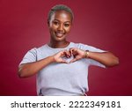 Small photo of Hands, heart and love with a model black woman in studio on a red background to promote health or wellness. Portrait, smile and hand sign with a young female posing to endorse romance or cardio