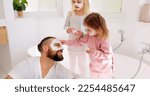 Small photo of Skincare, father and bonding with children or little girls in home bathroom. Fun, loving and caring dad bond with daughter siblings while applying face mask for smooth, glowing and healthy skin
