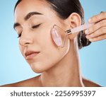 Skin care, face roller and beauty woman with facial massage for dermatology, cosmetic and wellness. Young aesthetic model person for natural rose quartz spa product to relax on blue background