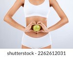 Small photo of Digestion, apple and woman stomach with hands in heart shape for nutrition, detox diet and studio background. Fruits, wellness and healthy abdomen body with care, love and lose weight for strong gut
