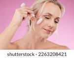 Face roller, beauty and woman facial massage with dermatology and cosmetic tools. Happy mature person on pink background for skincare, self care and rose quartz results for anti aging, glow and shine