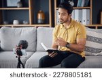 Small photo of Podcast, bible study and phone with a man online to preach or reading while live streaming. Asian male on home sofa with Christian scripture or book as content creator teaching on education religion