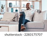 Tablet, coffee break and relax with a black man on the sofa, sitting in the living room of his home or office. Business, tech or research with a male employee reading an online article while chilling