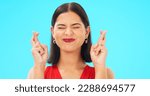Small photo of Happy, woman and face with fingers crossed on blue background, studio and wishing for good luck. Portrait of excited female model hope for winning prize, optimism and smile for emoji, hands and sign