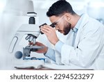 One serious medical scientist sitting at a desk and using a microscope to examine and analyse test samples on slides. Hispanic healthcare professional discovering a cure for diseases in his laboratory