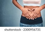Small photo of Heart, fitness and hands of a woman on a stomach isolated on a dark background in studio. Wellness, gut health and a girl with shape for love of body, weight loss and abdomen digestion on backdrop