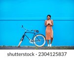 Small photo of Bicycle, young woman with smartphone and happy outside by blue wall. Cycling in urban area, health wellness and female person on cellphone outdoors standing in streets with bike or cycle in road