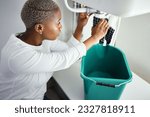 Small photo of Plumbing, water and a black woman in the bathroom of her home with a cloth and bucket waiting for assistance. Sink, emergency and burst pipe with a young female homeowner in her house to stop a leak