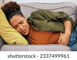 Small photo of Sick woman, stomach pain and problem on sofa for ibs, health risk or nausea of gastric bloating, period cramps or virus. Black female person, menstruation or stress of constipation from endometriosis