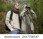 Couple, travel and binoculars in nature for hiking, adventure and journey or explore together in winter. Happy man and woman trekking with outdoor search, vision or birdwatching in forest or woods