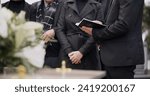 Small photo of Bible, hands and family at funeral, cemetery or burial ceremony religion by coffin tomb. Holy book, death and grief of people at graveyard, Christian priest reading spiritual gospel and faith in God