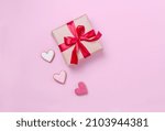 Beige gift box with a beautiful red bow on a pink flatlay background. A gift with a satin ribbon and hearts with a place for text. Beautiful concept for Valentine's Day