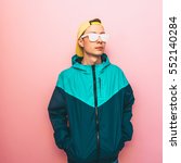 Small photo of fashion male model standing in the turquoise jacket, cap and sunglasses. clothing in the style of the 90s and the rave. minimal.
