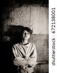 Small photo of Atmospheric monochrome image of an intense staring young boy constrained in a straight jacket leaning against on old cement wall in a retro lunatic asylum or psychiatric clinic