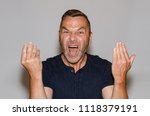 Small photo of Furious vehement middle-aged man yelling at the camera gesturing with his hands in rage in a communication concept against a studio background