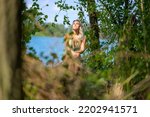 Small photo of Attractive blond woman wearing a gold gogo dress enjoying the sun on a tree trunk at the edge of a lake