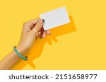 Small photo of Beautiful groomed womans hand with fashionable holding business card on yellow background