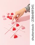 Small photo of Female hand playing tic tac toe game with heart shaped candies on pink background