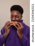 Small photo of Hungry black man bites very big piece of pizza, has appetite, enjoys eating fast food in office