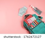 Small photo of COVID-19 prevention while going back to school and new normal concept.Top view of backpack with school supplies , blue polka dot fabric masks and sanitizer gel on pink background.
