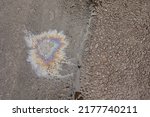Small photo of A patch of spilt oil has mixed with rain to show iridescent rainbow colours on a road surface