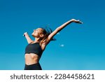 Horizontal portrait of a beautiful young fit smiling woman deep breathing in front of a clear blue sky in a sunny windy day of summer