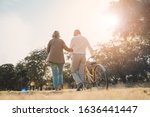 Beautiful Senior couple walking their bike along happily talking in park.mature couple in summer park.Elderly man and old woman with bicycles outside in spring nature.