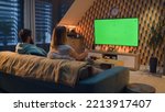 Small photo of Woman switching channels with remote control. Couple sitting on couch in living room, talking, watching breaking news, movie or series on TV. Resting at home in the evening. Green screen. Chromakey.