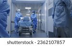 Small photo of Nurse and paramedic open medical facility corridor doors. Multi ethnic surgeons push stretcher with lying elderly patient to operating room. Medical personnel work in emergency department