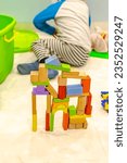 Small photo of Unrecognizable kid in his room at home rear view from his back head decapitated and an unbalanced wooden building blocks construction that holds together. Focus on foreground with blurred background.