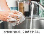 Small photo of Young woman's hands washing a white cup with water and dish soap. Close-up of female hands rinsing a dirty used white mug with the tap running. Concept of cleanliness