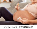 Small photo of Mature pregnant woman puting injection on her belly at home. Woman on her 40s injecting anticoagulant on her abdomen to avoid clot problems on pregnancy