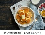 Small photo of Pancakes cereal, tiny thin funny crumpet, children's food. Breakfast with drink, dark table, bright morning, top view, copy space
